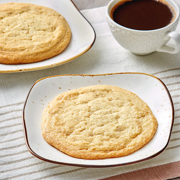 A plate with two David's Cookies sugar cookies next to a cup of coffee.