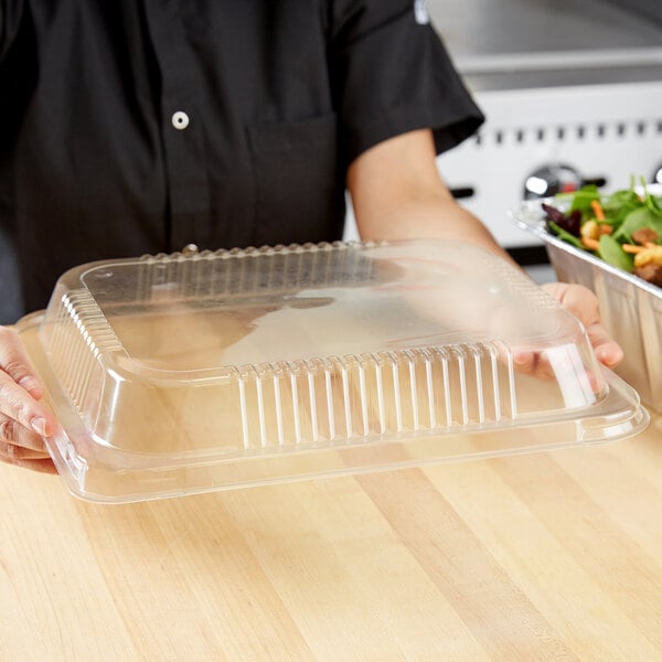 A person holding a clear plastic container with a Durable Packaging half size dome lid on top.