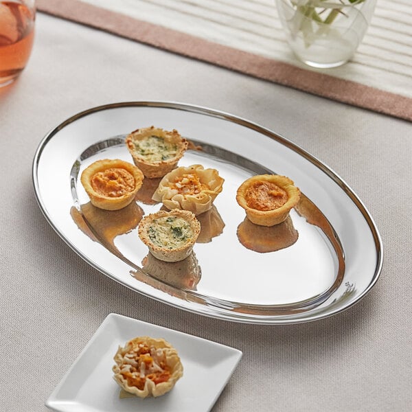 An Acopa stainless steel oval platter with small appetizers on a table.