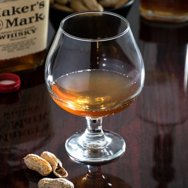 A Libbey brandy glass filled with liquor on a table with peanuts.
