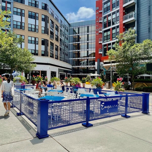 A blue SelectSpace patio fence with people sitting around it on a outdoor patio.