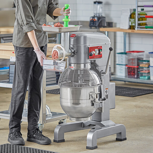 A woman using an Avantco floor mixer with a meat grinder attachment to grind meat.