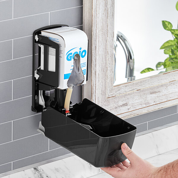 A hand using a GOJO hand soap dispenser to fill a sink.