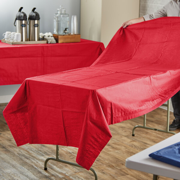 A person holding a red Hoffmaster tablecloth over a table.