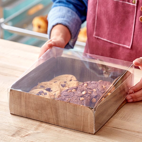 A person holding an Enjay wood laminated take-out box filled with cookies.