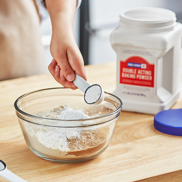 A person adding Double Acting Baking Powder to a bowl of flour.