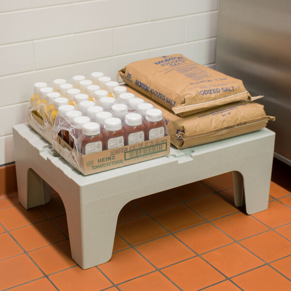 A white table with a plastic container of ketchup and a package of brown bags on a Cambro solid top dunnage rack.