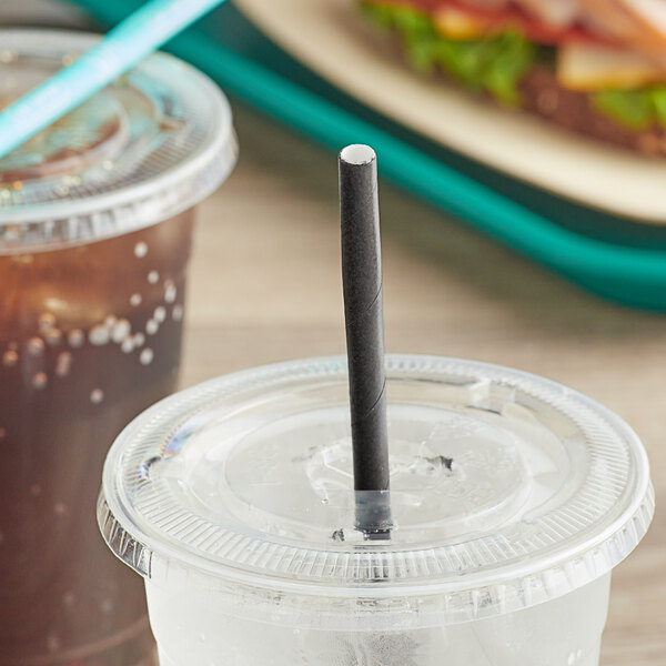 A plastic cup with a SOFi black paper straw in it on a table.