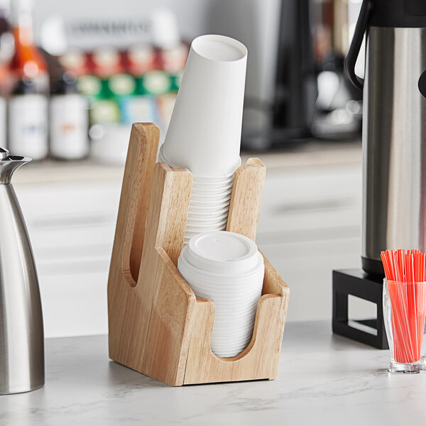 A wooden Acopa cup and lid organizer on a counter holding cups and straws.