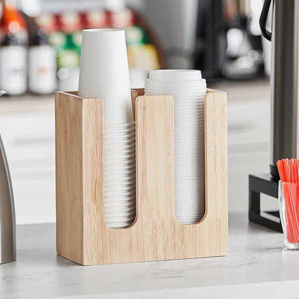 A wooden Acopa cup and lid organizer on a counter with cups and straws.