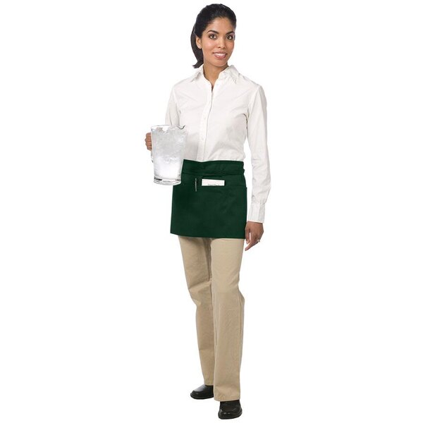 A woman wearing a Chef Revival hunter green waist apron with 3 pockets.