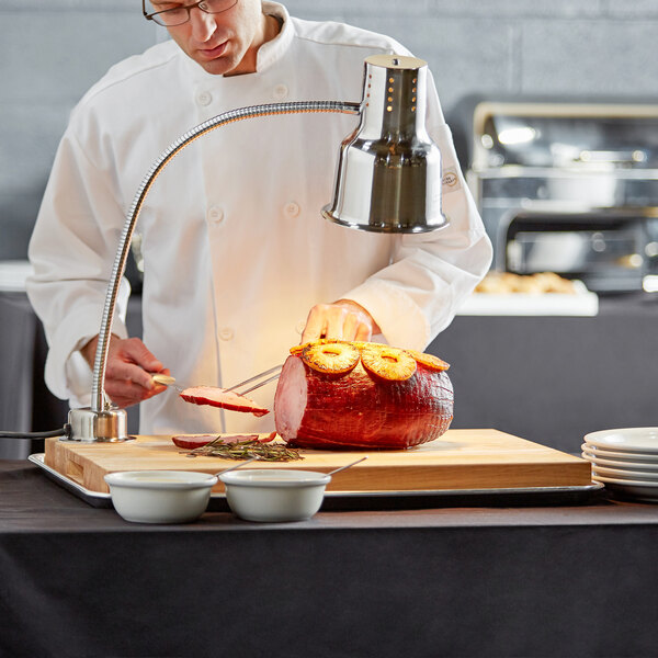 An Avantco wood cutting board on a table with a chef slicing a piece of meat.