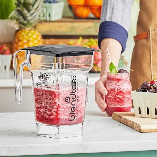 A person holding a Blendtec clear jar filled with red smoothie.