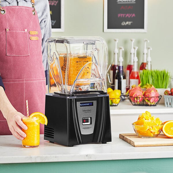 A person in an apron using a Blendtec Connoisseur 825 blender to make an orange drink.