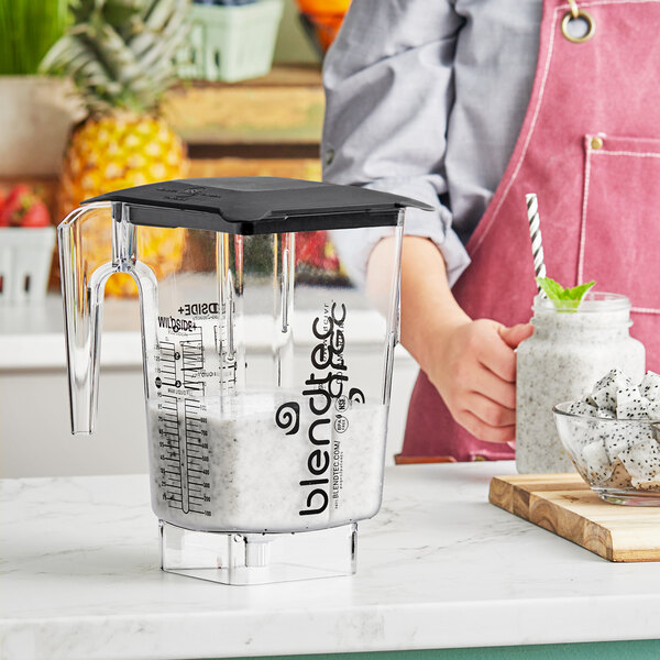 A woman using a Blendtec blender with a clear jar filled with a white smoothie.
