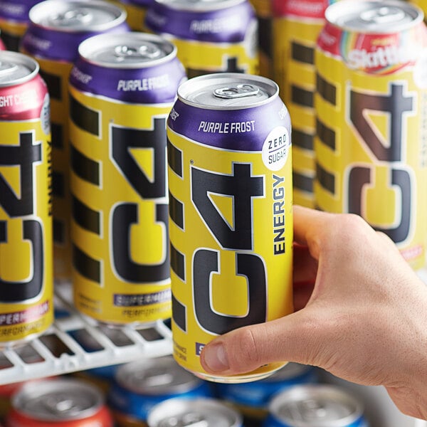 A hand holding a yellow and black C4 Energy Purple Frost energy drink can.