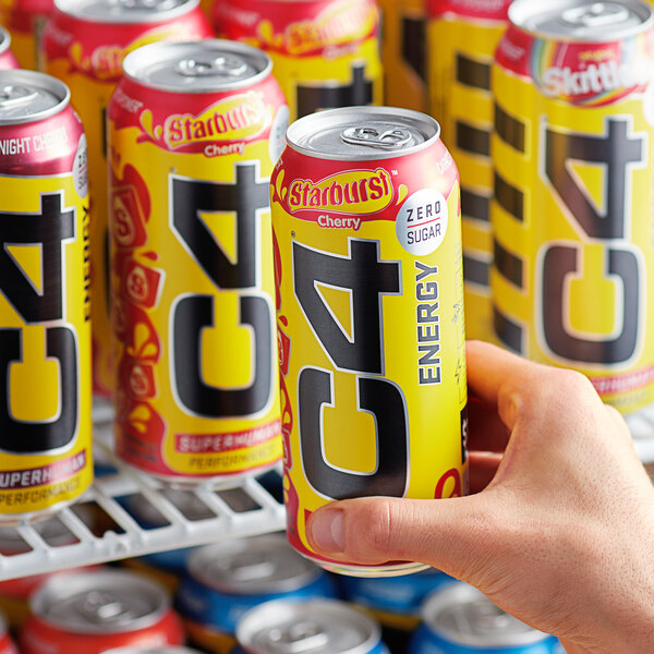 A person's hand holding a yellow C4 Energy drink can with black and red accents.