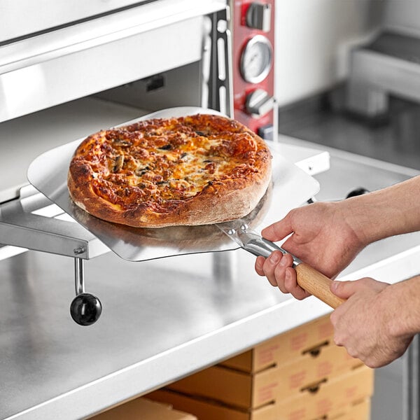 A person using a Choice aluminum pizza peel to remove a pizza from a pizza oven.