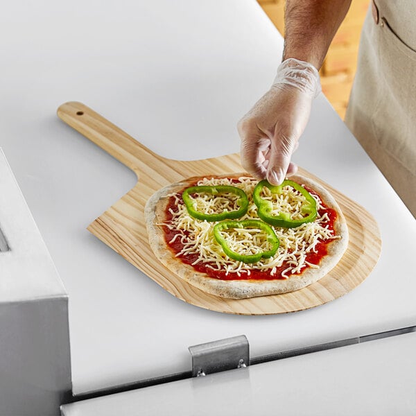 A person using a Choice wooden pizza peel to transfer a pizza to a counter.