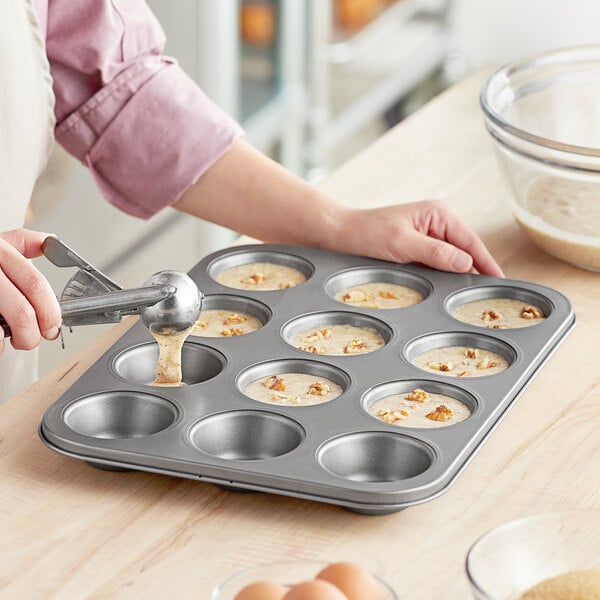 A woman pouring batter into a Choice carbon steel muffin pan.