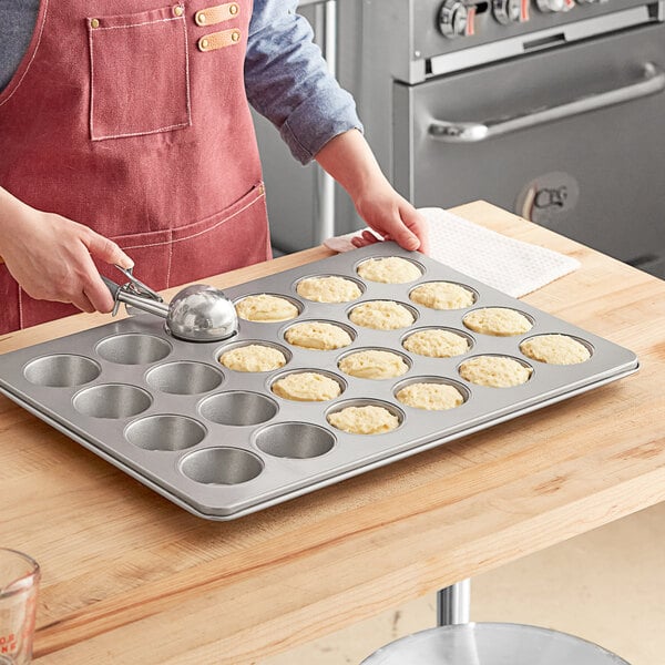 A person in an apron putting food into a Choice muffin pan.