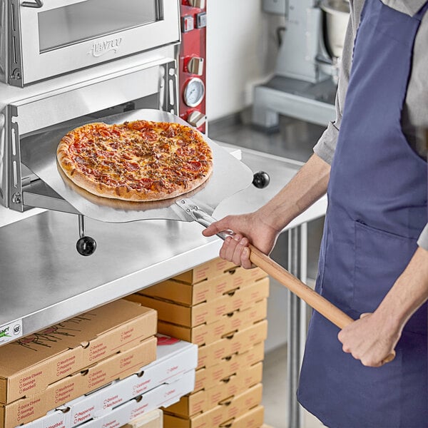 A man using a Choice aluminum pizza peel to put a pizza in the oven.