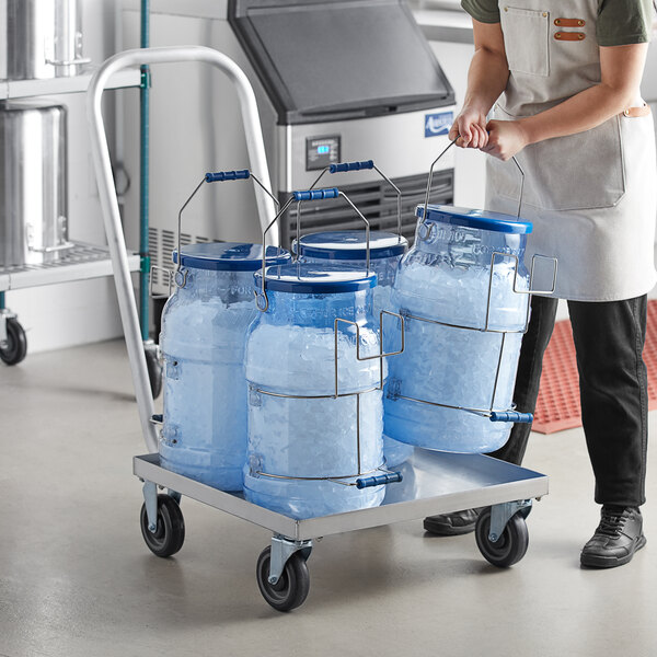 A woman in a white apron pushing a cart with blue Vigor ice totes on an aluminum dolly.
