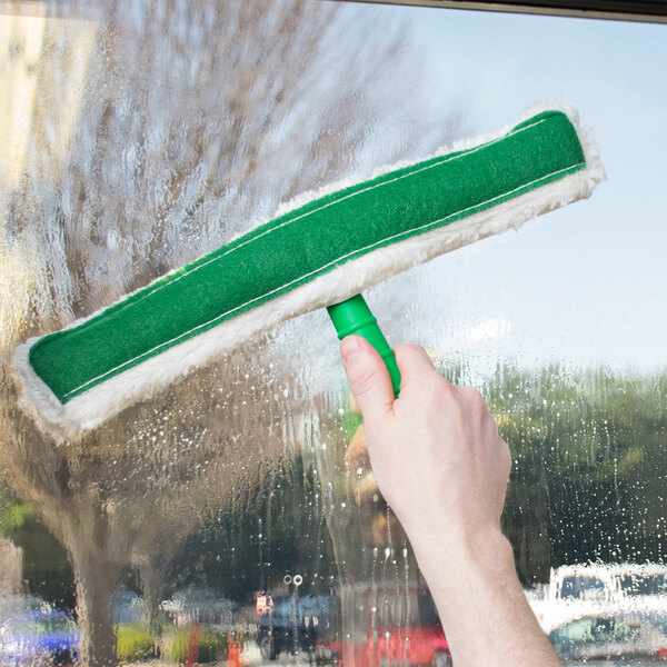 A person using an Unger ThePad StripWasher with a green and white T-Bar to clean a window.