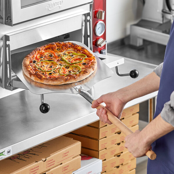 A man using a Choice aluminum pizza peel to cook a pizza in a pizza oven.