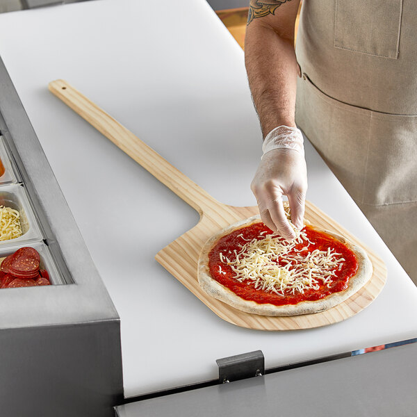 A person using a Choice wooden pizza peel to put a pizza in the oven.