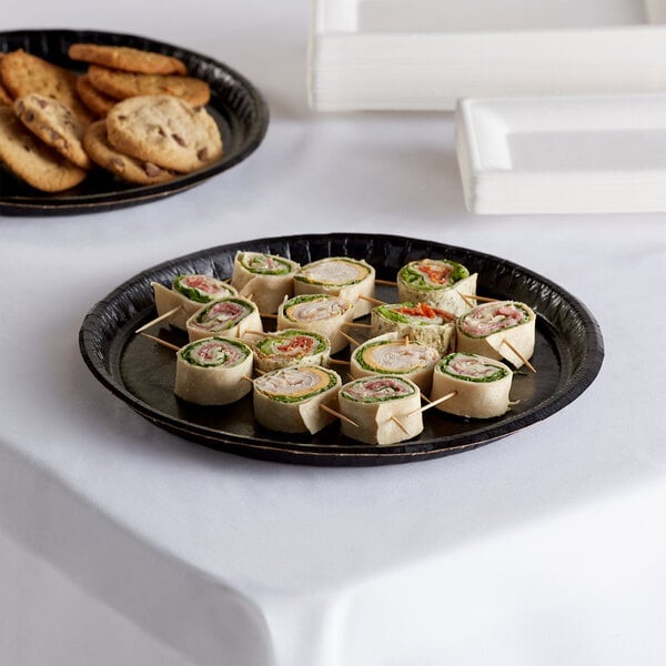 A Solut round black catering tray with a sandwich and cookies on it.