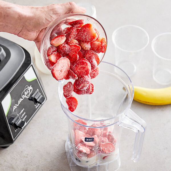 Sliced strawberries being poured into a blender with bananas.
