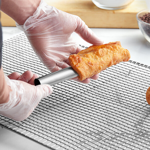 A hand holding a stainless steel Ateco cannoli mold.