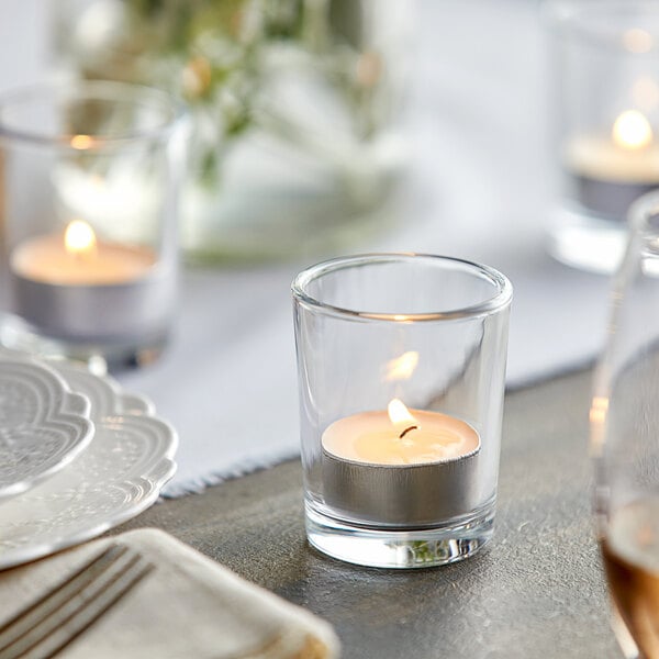 A table setting with a candle in a clear glass votive holder.
