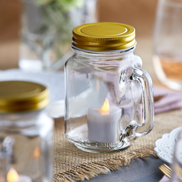 An Acopa Mason candle jar with a lit candle inside sitting on a table.