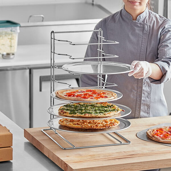 A woman using a Choice 7 Slot Pizza Pan Rack to hold pizzas.