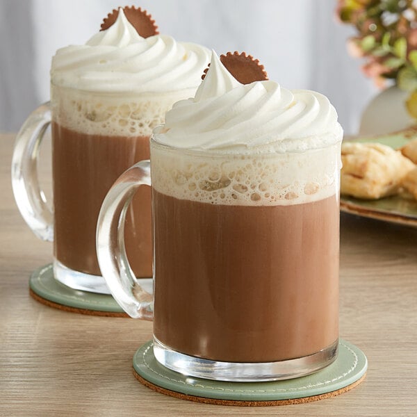 Two mugs of Land O Lakes Peanut Butter and Chocolate hot chocolate with whipped cream and chocolate drizzle.