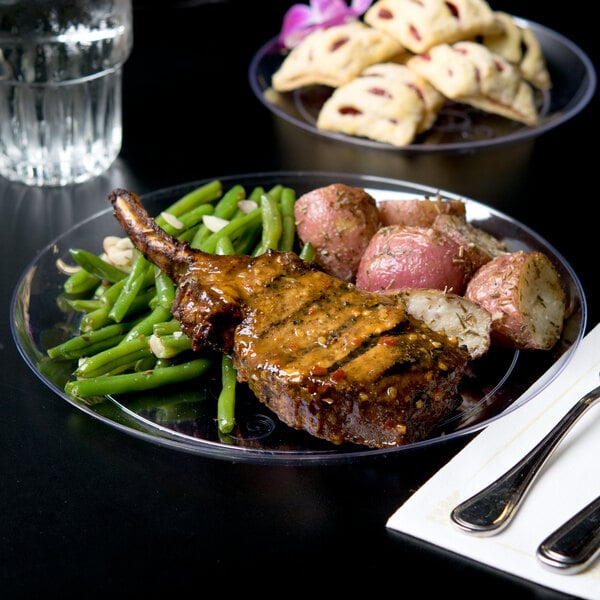A Fineline clear plastic plate with meat, potatoes, and green beans on a table.
