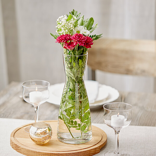 An Acopa glass vase with water, leaves, and flowers on a wooden tray.