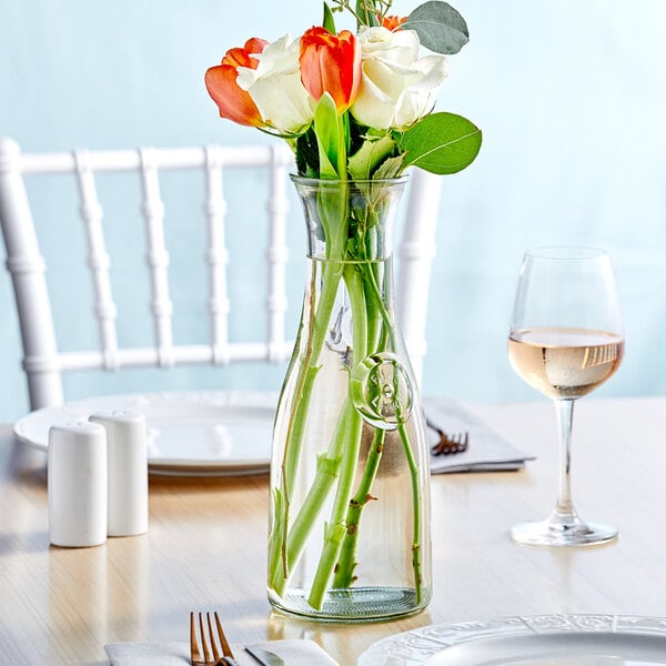 An Acopa farmhouse glass vase with flowers on a table in a restaurant.