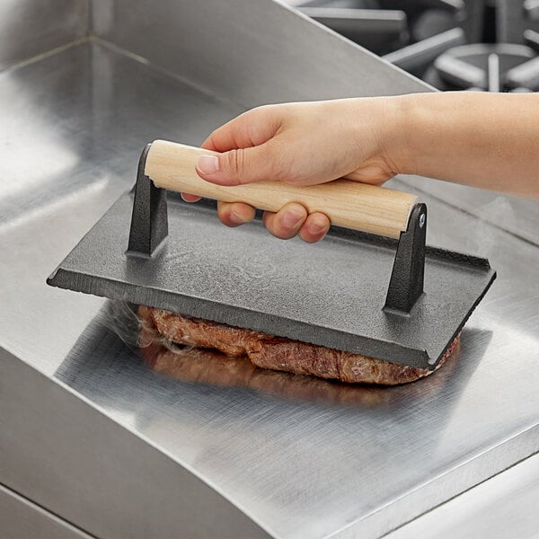 A hand using a Choice cast iron steak weight to press a meat patty on a metal surface.