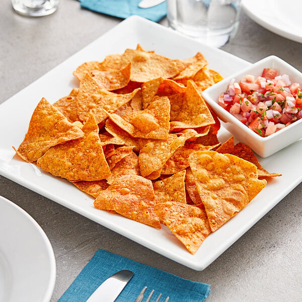 A plate of Mr. Tortilla Low Carb Chile Limon tortilla chips with a bowl of salsa on a table.