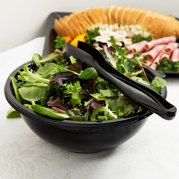 A bowl of salad in a black Fineline PET plastic bowl with black tongs.