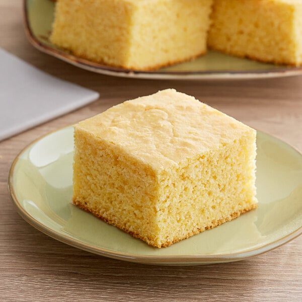 A piece of square yellow cornbread on a green plate.