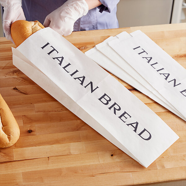 A person putting a bag of Italian bread into a white paper bag.
