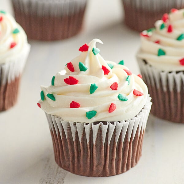 A chocolate cupcake with white frosting and red and green Christmas tree sprinkles.