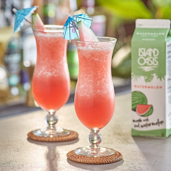 Two glasses of Island Oasis watermelon drinks with straws on a table.