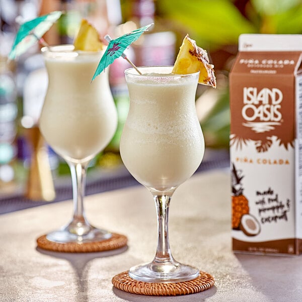 Two glasses of Island Oasis Pina Colada drink with umbrellas and pineapples.