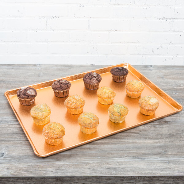 A Chicago Metallic bakery display tray with brown muffins on a wooden table.