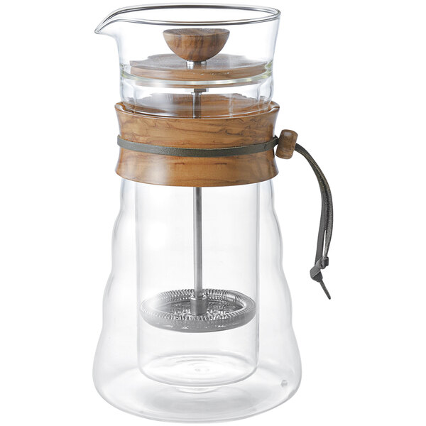 A Hario glass and olive wood coffee maker on a table.